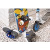 La imagen muestra un monopatín colorido apoyado en una pared de piedra, junto a un patinete. Hay zapatos deportivos grises y azules tirados sobre grava blanca.