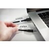 La imagen muestra una mano que sostiene una etiqueta con el nombre 'ANNA' juntando cables que están conectados a una computadora portátil con una etiqueta 'KAMERA'.