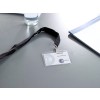 En la imagen hay una etiqueta de visita con un cordón negro, que muestra la palabra 'VISITEUR' y el nombre 'Abella Boulet' sobre una mesa. También hay un vaso de agua y un bloc de notas al fondo.